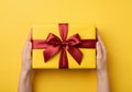 Hands holding a beautifully wrapped yellow gift box with a red ribbon Royalty Free Stock Photo