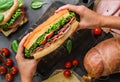 Hands holding big sandwich with ham, bacon, cheese, lettuce, tomatoes, sausage, gammon