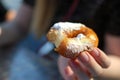 Hands holding bited donut dusted with powdered sugar close up.