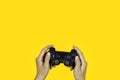 Hands holding a black joystick, game controller isolated on yellow background