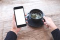 Hands holding black mobile phone with blank white desktop screen and a cup of coffee on wooden table in cafe Royalty Free Stock Photo