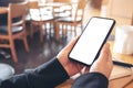 Hands holding black mobile phone with blank white screen horizontally with coffee cup on wooden table in vintage Royalty Free Stock Photo