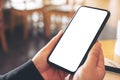 Hands holding black mobile phone with blank white screen horizontally with coffee cup on wooden table in vintage Royalty Free Stock Photo