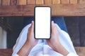 Hands holding black mobile phone with blank white screen horizontally with coffee cup on wooden table in vintage Royalty Free Stock Photo