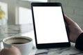 Hands holding black tablet pc with white blank screen and coffee cup on table background Royalty Free Stock Photo