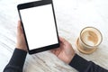 Hands holding black tablet pc with white blank screen and coffee cup on table background Royalty Free Stock Photo