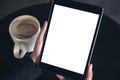 Hands holding black tablet pc with white blank screen and coffee cup on table background Royalty Free Stock Photo