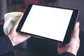 Hands holding black tablet pc with white blank screen and coffee cup on table background Royalty Free Stock Photo