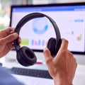 Hands Holding Black Wireless Headphones in Front of Computer Monitor at Workplace Royalty Free Stock Photo