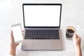 Hands holding blank mobile phone and coffee cup while using laptop with blank white screen on table Royalty Free Stock Photo