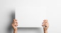 Hands holding a blank white rectangular paper or card horizontally against a white wall with soft shadow for messages Royalty Free Stock Photo