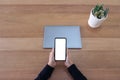 A hands holding a blank white screen mobile phone and laptop on wooden table in office Royalty Free Stock Photo