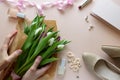 Hands holding bouquet of white and purple tulips. Feminine accessories and blank paper on pink background. Top view. Flat lay. Royalty Free Stock Photo