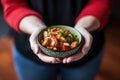 hands holding a bowl of kung pao chicken close-up