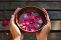 hands holding a bowl of water with floating rose petals