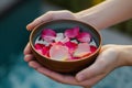 hands holding a bowl of water with floating rose petals