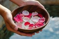 hands holding a bowl of water with floating rose petals