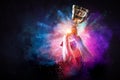 Hands holding champion cup on colourful splashes background. Mixed media Royalty Free Stock Photo