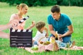 Hands Holding Clapperboard While Family Enjoying Picnic On Field