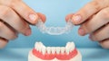 Hands holding clear dental aligner over teeth model on blue background image Royalty Free Stock Photo