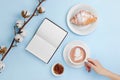 Hands holding coffee and notebook with croissant and cotton branch