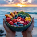 Hands holding a colorful fruit bowl by the seaside at sunset. Royalty Free Stock Photo