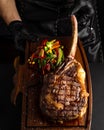 Hands holding cooked Tomahawk steak on a serving board. Low key image, vertical orientation