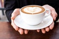 Hands holding cup of hot coffee latte with heart shaped foam art