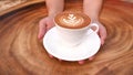 Hands holding a cup of hot latte cappuccino coffee on wooden table