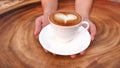 Hands holding a cup of hot latte cappuccino heart shape foam coffee on wood table