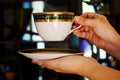 Hands holding a cup of steaming beverage and a saucer