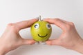 Hands holding cute little Apple with Googly eyes and drawn smile. Apple haracter on white background