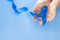 Hands holding deep blue ribbon on blue background with copy space. Colorectal Cancer Awareness Colon cancer of older person and
