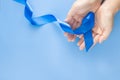 Hands holding deep blue ribbon on blue background with copy space. Colorectal Cancer Awareness Colon cancer of older person and Royalty Free Stock Photo