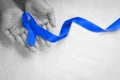 Hands holding deep blue ribbon on white fabric with copy space. Colorectal Cancer Awareness, Colon cancer of older person and