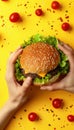 Hands holding delicious burger on bright yellow background for vibrant food concept