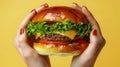 Hands holding delicious burger on vibrant yellow background for enticing food concept
