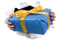 Hands holding delivering or giving small Christmas or birthday gift surprise through torn white paper background