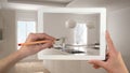 Hands holding and drawing on tablet showing blurry modern kitchen. Real finished minimalist white and wooden kitchen in the backgr