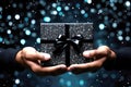 Hands holding elegant luxury present gift box with black ribbon bow on black background. Shopping boxing day