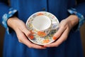 hands holding a fine china cup and saucer with a floral pattern