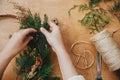 Hands holding fir branches and pine cones, berries, thread, scissors on wooden table. Making rustic christmas wreath flat lay. Royalty Free Stock Photo