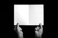 Hands holding folded blank sheet of paper against black background Royalty Free Stock Photo