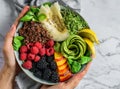 Hands holding fresh summer salad with quinoa, peach, micro greens, avocado, berries, coconut, melon on light marble background. Royalty Free Stock Photo