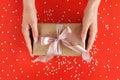 Hands holding gift box wrapped in kraft paper with satin ribbon on festive red background. Xmas, New Year postcard Royalty Free Stock Photo