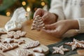 Hands holding gingerbread cookie tree with icing on rustic wooden table. Atmospheric Christmas holiday traditions, family time. Royalty Free Stock Photo