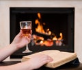 Hands holding glass of cognac and book by the fireplace Royalty Free Stock Photo