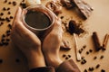 Hands holding glass cup with fresh coffee and roasted beans,ground coffee on spoon, macarons, chocolate, cinnamon on brown Royalty Free Stock Photo