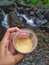 Hands holding glasses filled with coffee around river flows and rocks Royalty Free Stock Photo