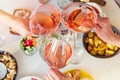 Hands holding glasses with rose wine over the table with food.